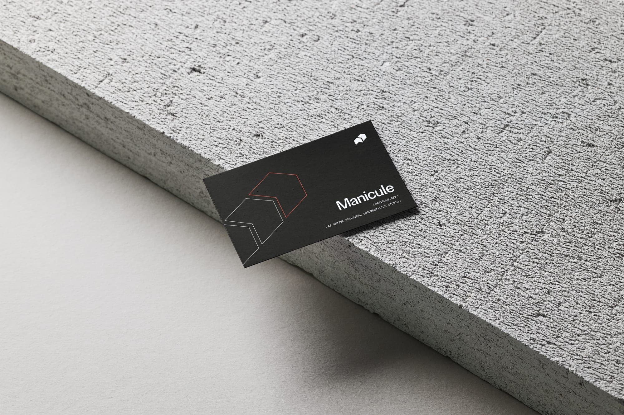 Business card front resting on concrete, mark and wordmark in soft white on charcoal.